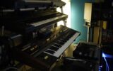 Mehrere Synthesizer und elektronische Geräte in einem abgedunkelten Musikstudio