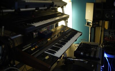 Mehrere Synthesizer und elektronische Geräte in einem abgedunkelten Musikstudio