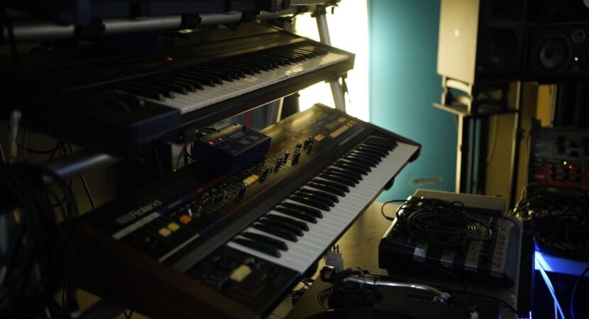 Mehrere Synthesizer und elektronische Geräte in einem abgedunkelten Musikstudio