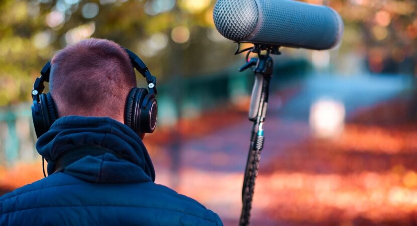 Person mit Kopfhörern vor einem Richtrohrmikrofon im Freien
